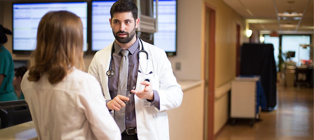 Male hospitalist speaks with another health care provider in hallway