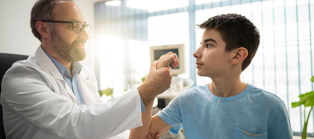 Male pediatrician examines the arm of a teen boy.