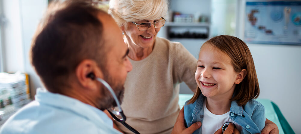 Male family physician listening to young girl’s heart with stethoscope.