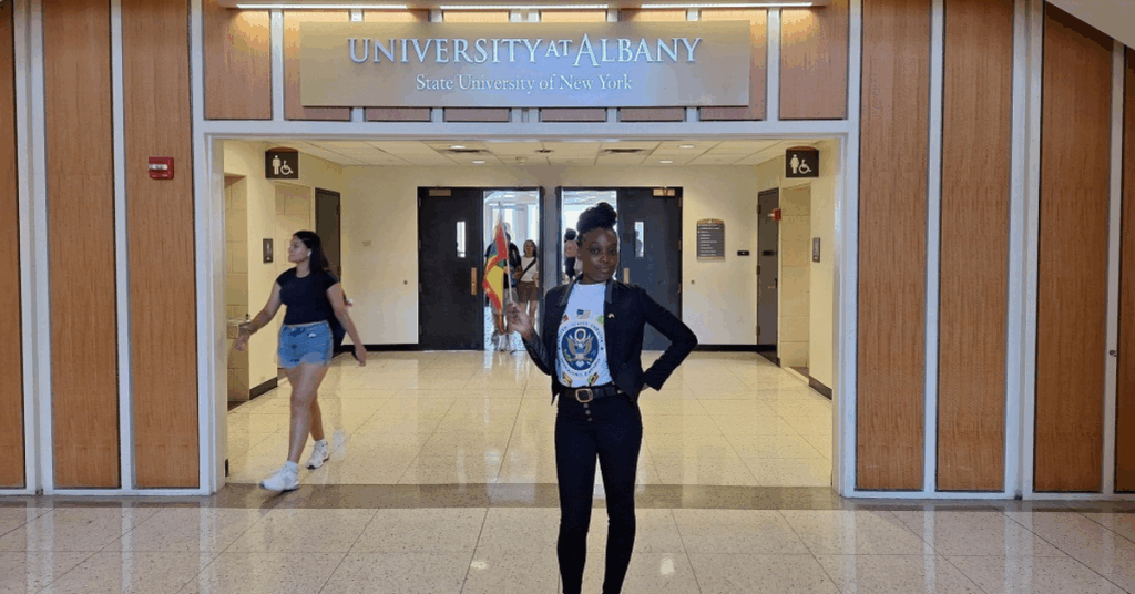 Alanda Joseph standing in front of "University at Albany sign"|Alanda Joseph standing in front of "University at Albany sign"