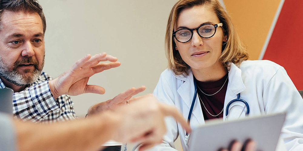 Female hospitalist speaks with a patient in hospital room.