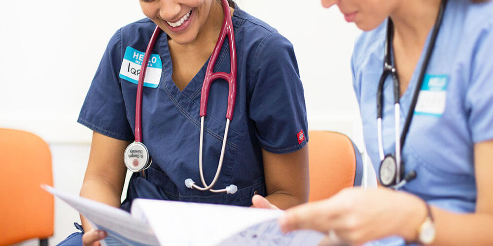Two SGU clinical ob/gyn students compare notes during a break in a hospital hallway.