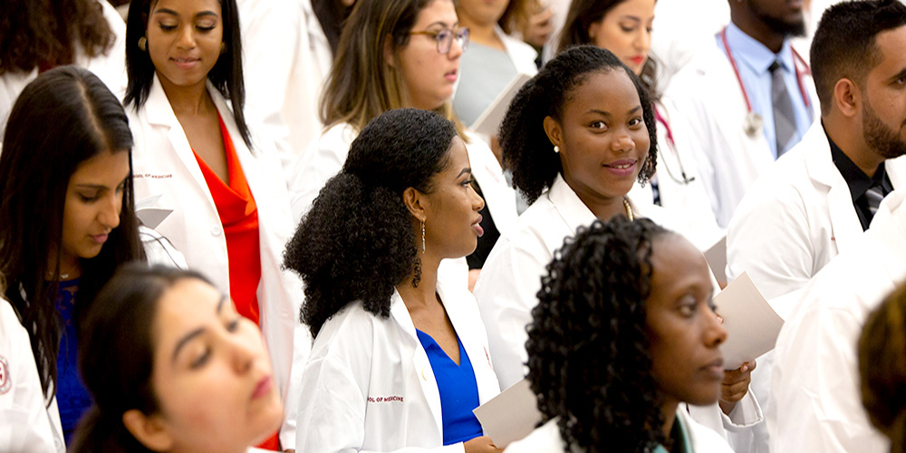 A large group of medical students stands together as the students recite an oath as part of the white coat ceremony to celebrate the start of their career journeys.