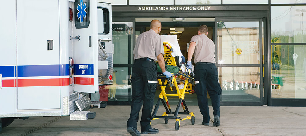 Two paramedics transport patient on stretcher from ambulance into emergency room